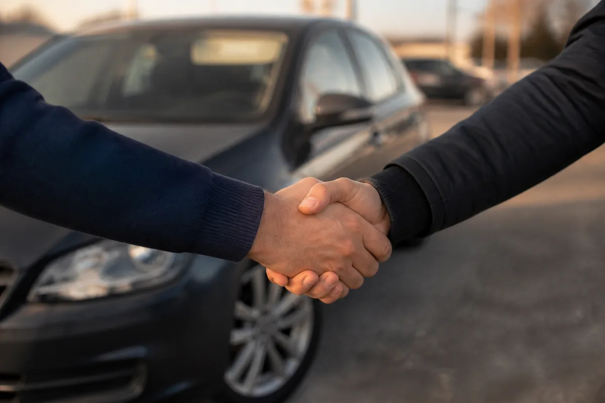 Poignée de main entre deux personnes devant une voiture d&rsquo;occasion